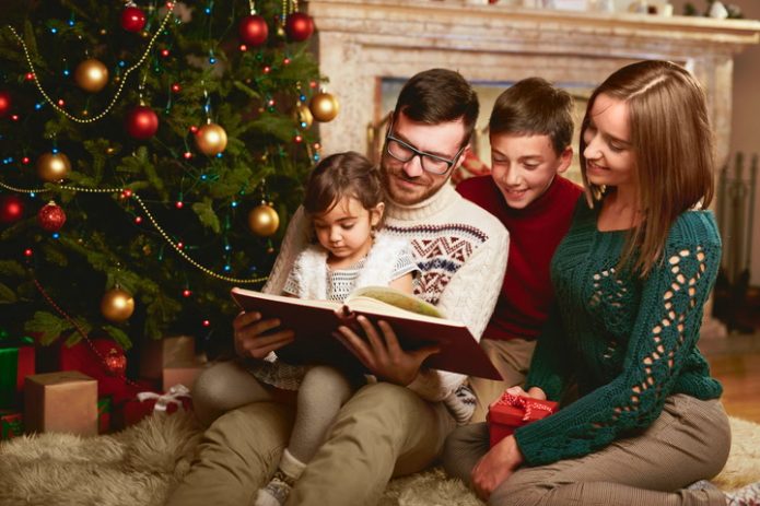 семья с детьми читает книгу возле новогодней ели